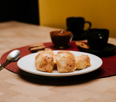 Tasty cheese bread rolls on a plate with coffee cups, creating a cozy atmosphere.