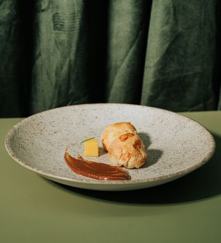 Elegant dessert presentation with gourmet pastries and chocolate sauce on a speckled plate against a green backdrop.