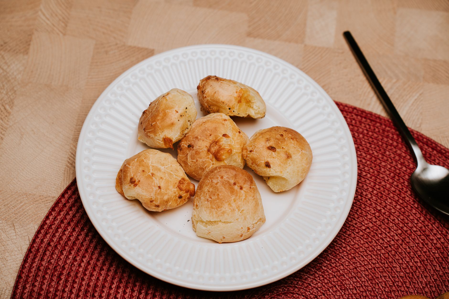 Sweet Summer Treats: Refreshing Drinks and Desserts A plate of fresh cheese buns served on a red placemat with a spoon beside.