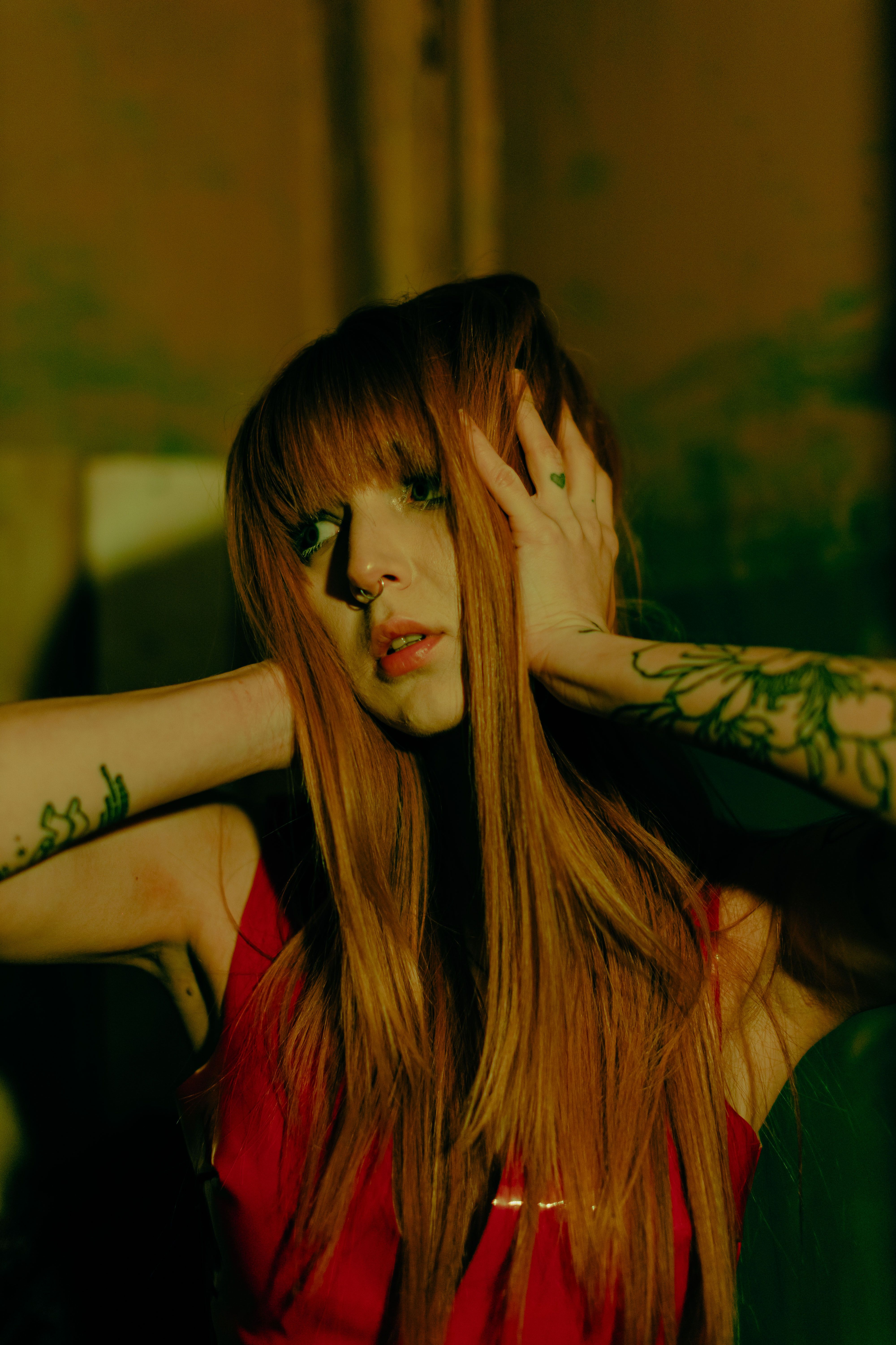 Intimate portrait of a tattooed woman with red hair under moody lighting.