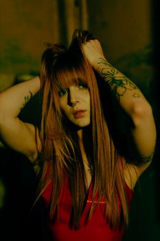 Moody portrait of a tattooed woman in dim lighting holding her hair.