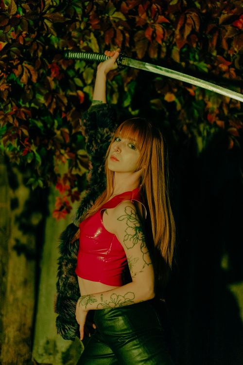 Free A tattooed woman stands confidently outdoors holding a sword under autumn leaves. Stock Photo