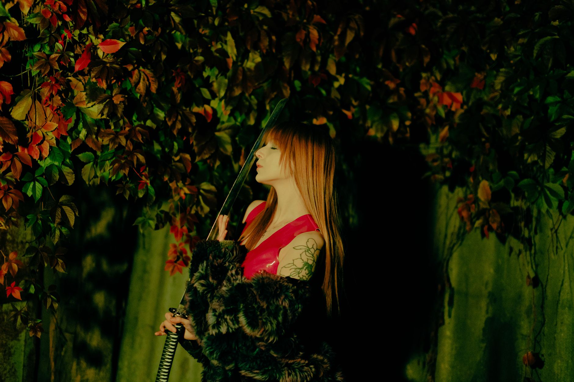 A woman in a red outfit with a katana surrounded by vibrant foliage.
