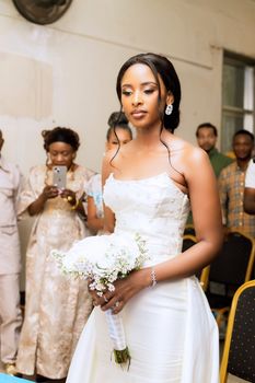 Beautiful bride in white gown holding bouquet during indoor wedding ceremony.