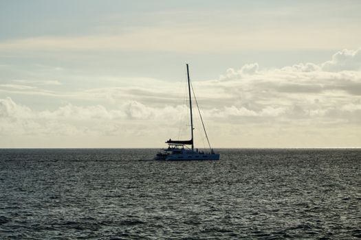 A solitary yacht gracefully sails on the tranquil ocean under a cloudy sky.
