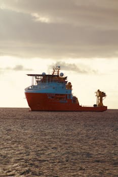 A bright orange cargo ship sails on a calm ocean under a cloudy sky during the day.