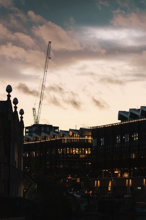 Free Evening cityscape featuring modern buildings and a construction crane during twilight. Stock Photo