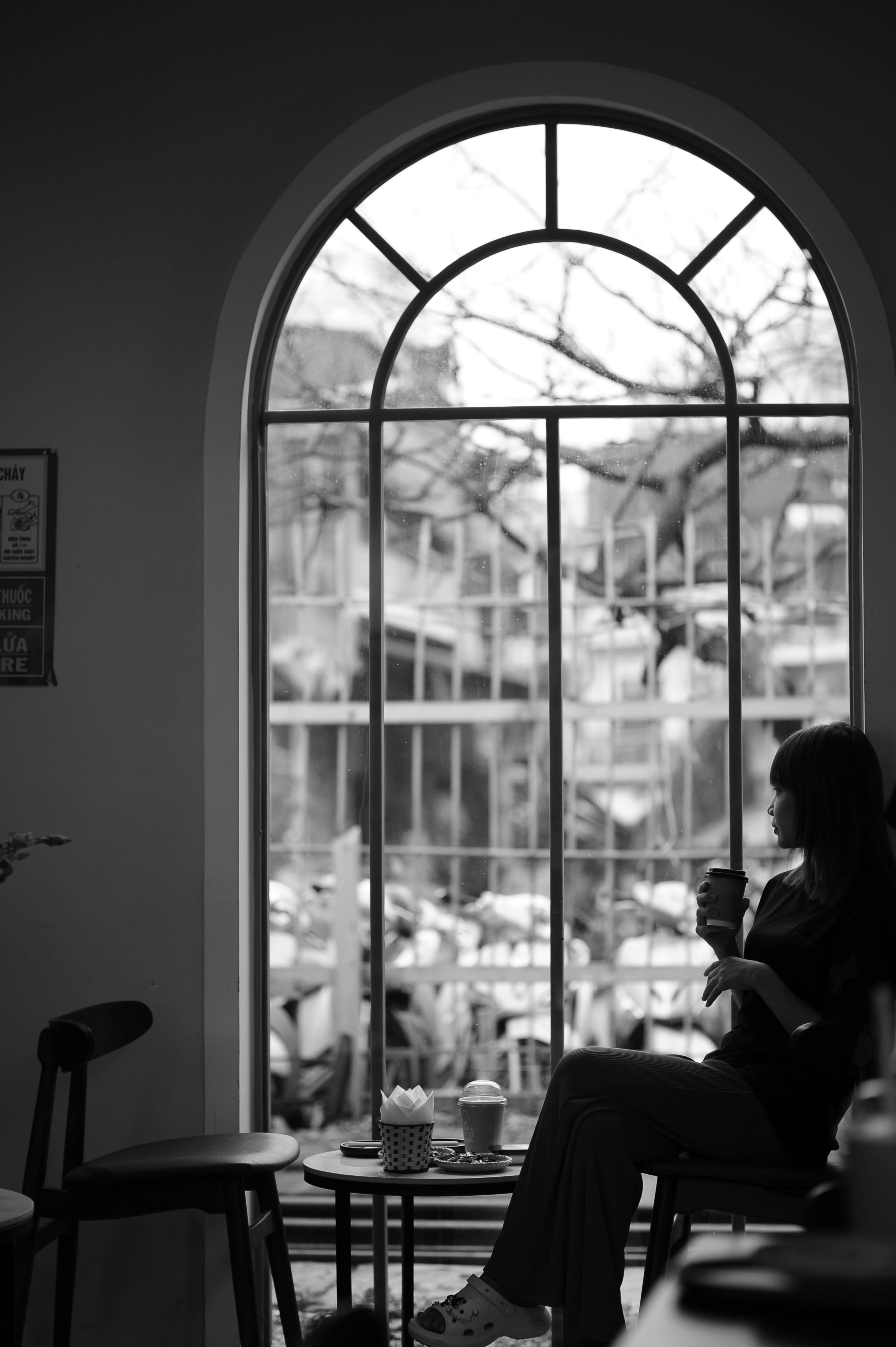 bezplatná Žena držící šálek kávy se dívá z velkého okna v útulném prostředí kavárny. Základová fotografie