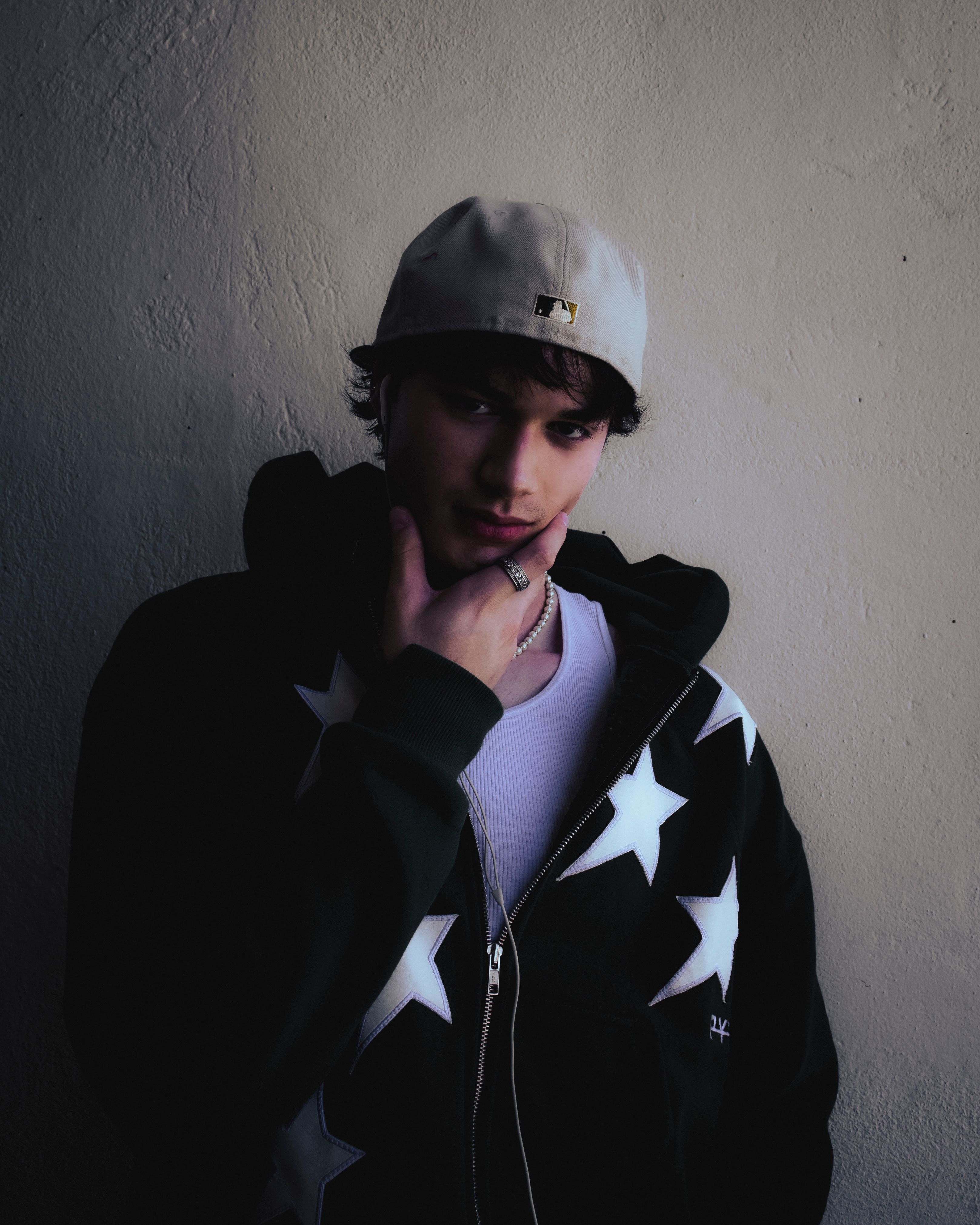 Young man posing in a star-pattern hoodie, wearing a baseball cap. Casual, modern style.