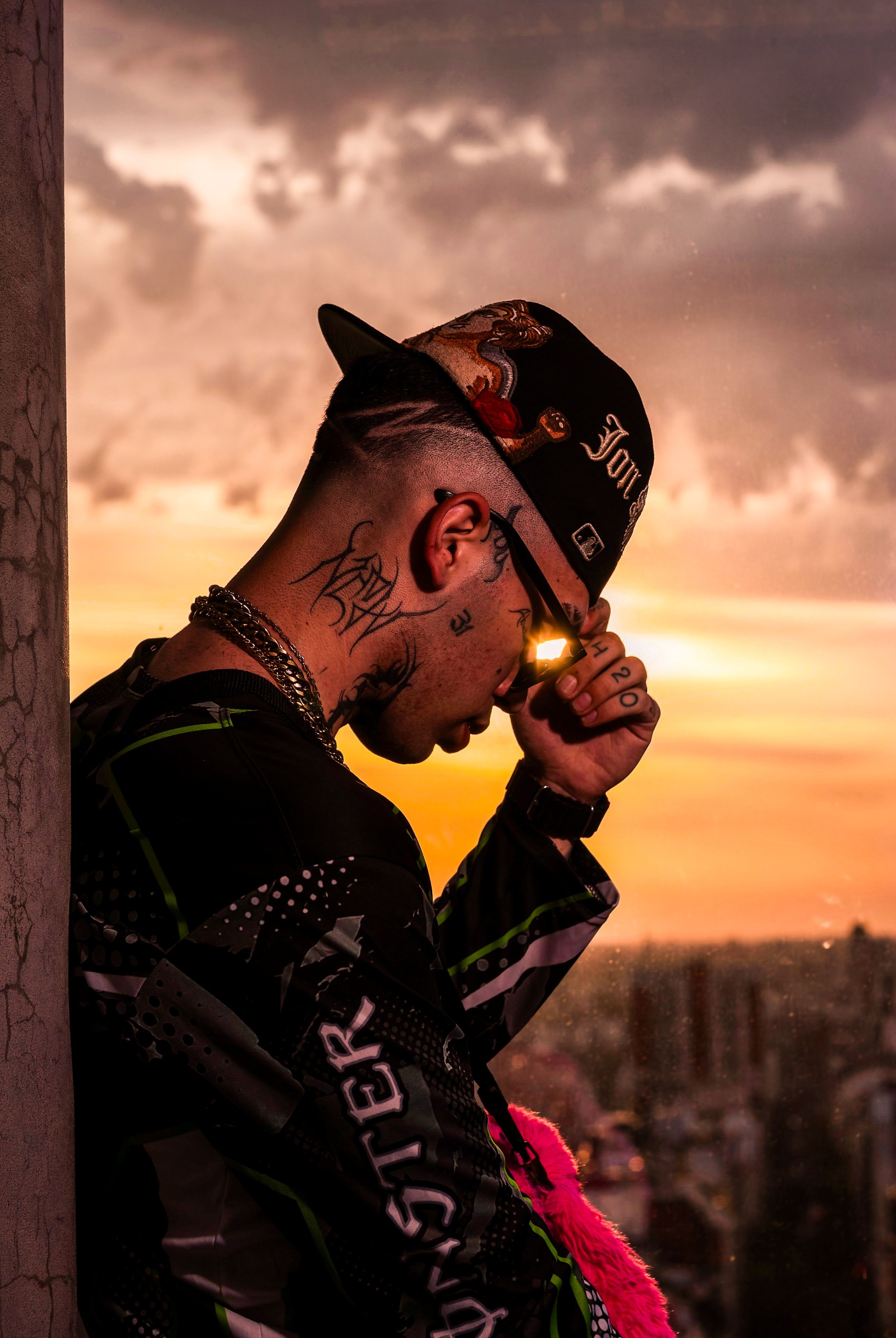 A pensive man stands against a wall at sunset in a cityscape.