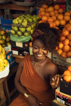 Joyful woman in orange dress surrounded by tropical fruits in an outdoor market.