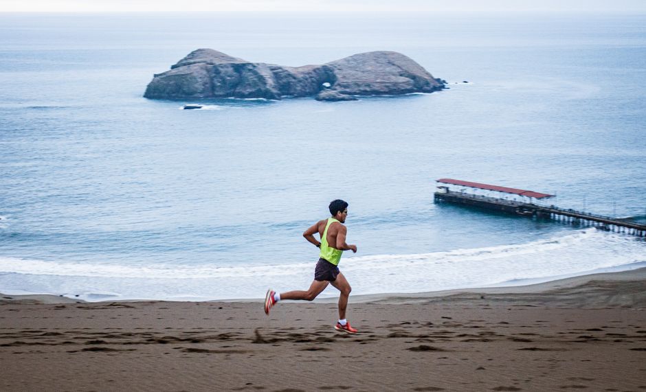 A man running on the sandy beach of Ventanilla, Callao, Peru with ocean views.