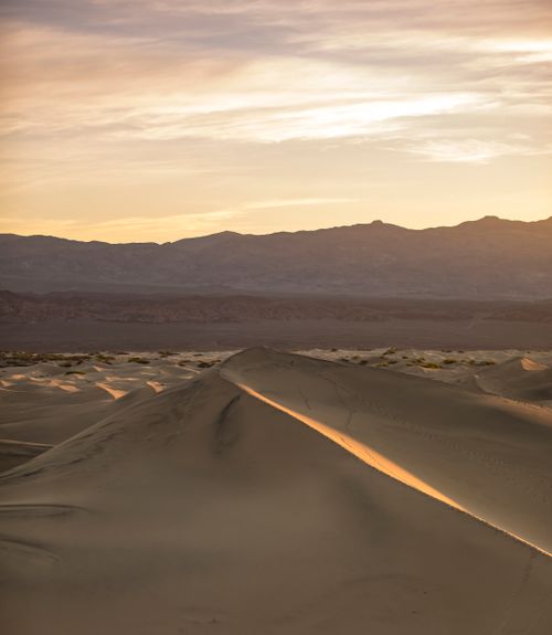 Free Beautiful sunrise over desert sand dunes with a mountain backdrop, showcasing serenity and vastness. Stock Photo