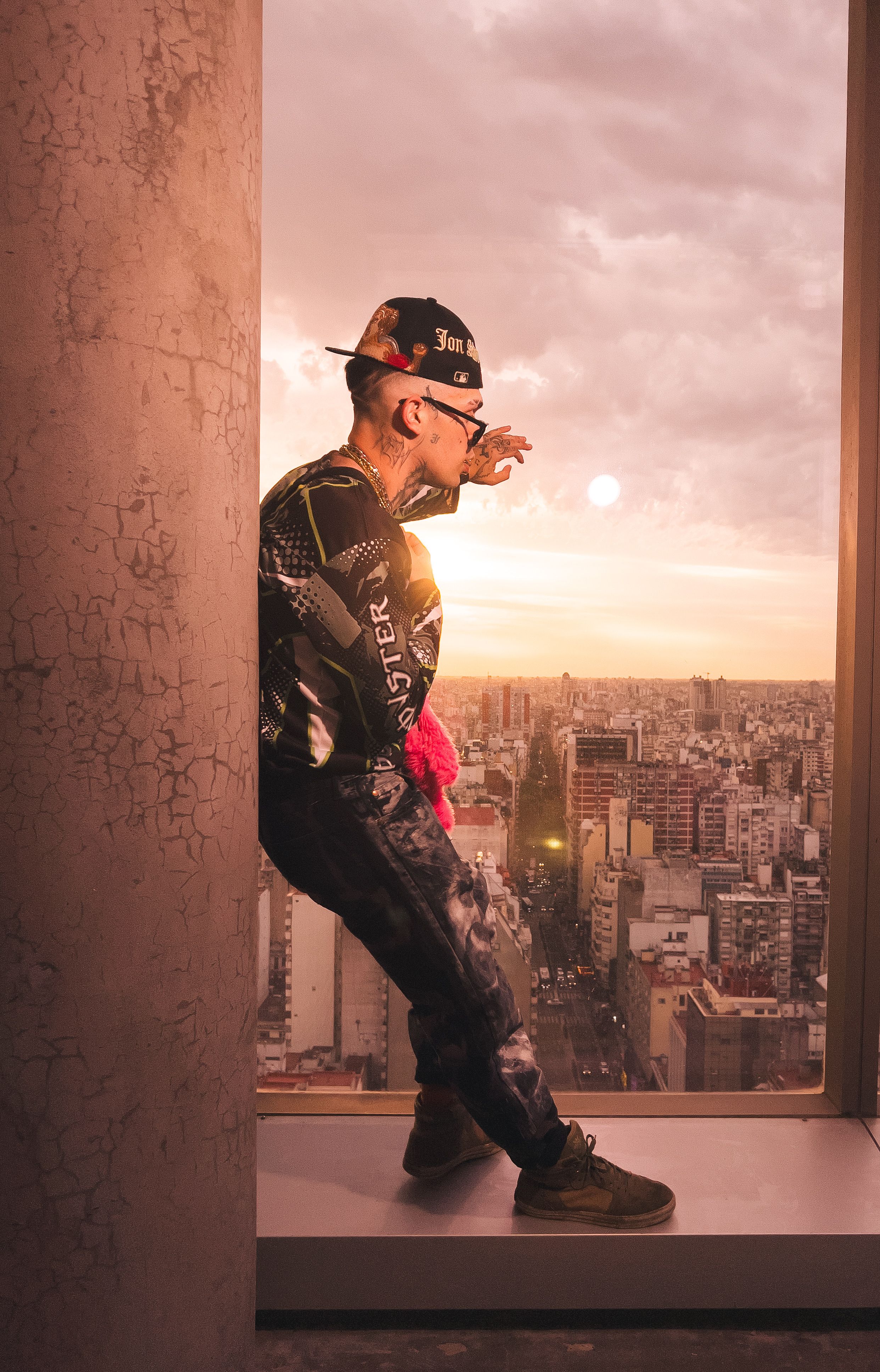 Trendy individual poses in urban window with sunset skyline view.