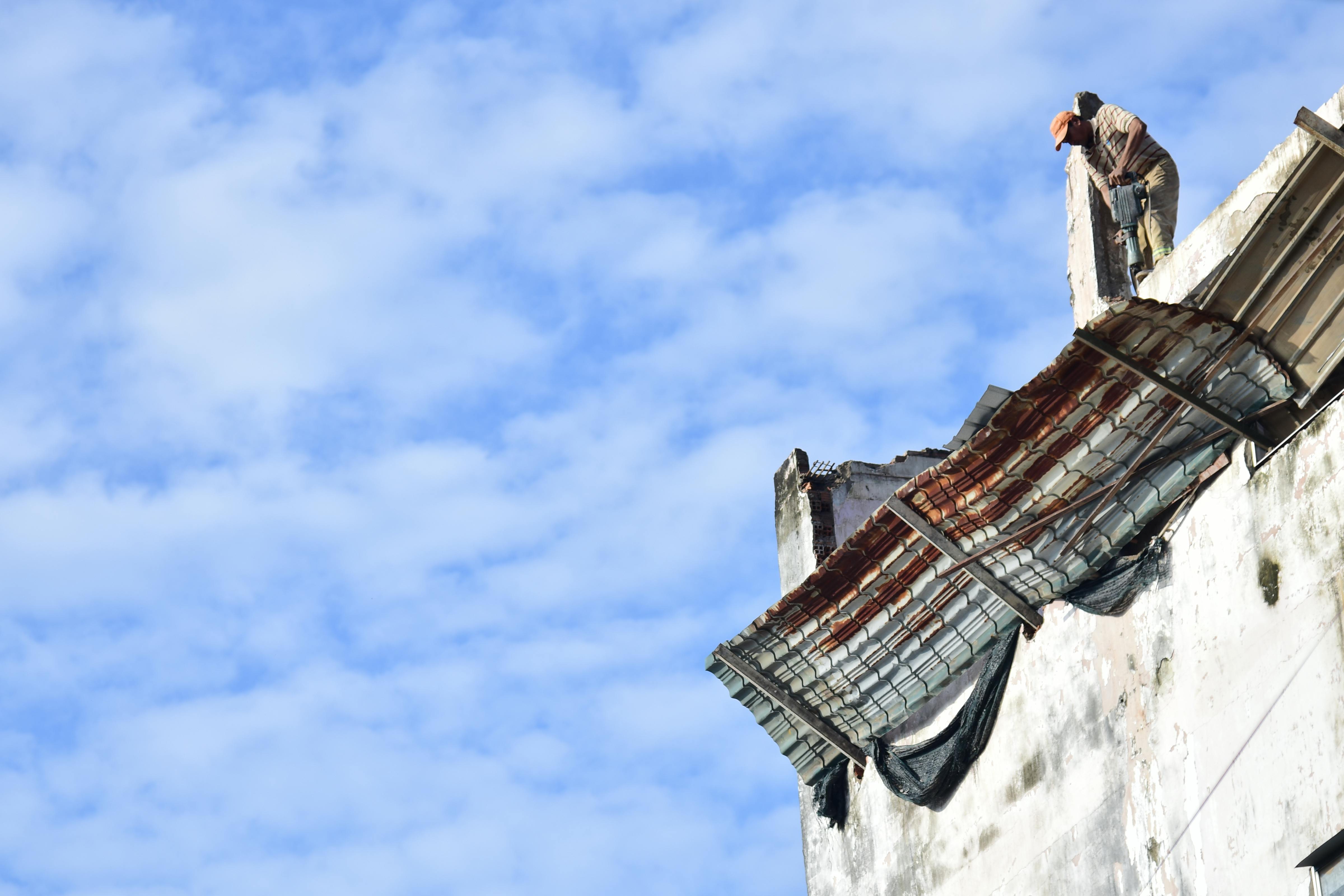 A construction worker repairing a roof on a bright, sunny day with blue sky.