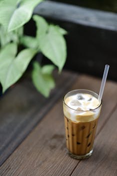 A refreshing glass of iced coffee with a straw on a rustic wooden table.