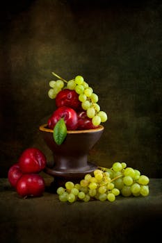 A classic still life of fresh grapes and plums in a rustic bowl, set against a moody background.