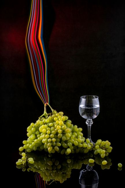 A small tulip glass of clear grappa next to a cluster of dark grapes and a rustic Italian bottle