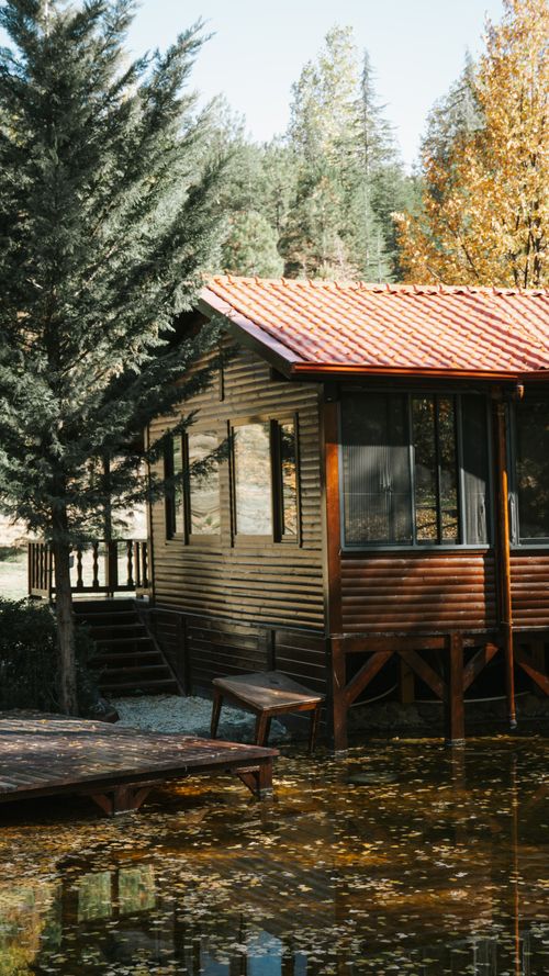 Free A charming wooden cabin by a serene lake surrounded by autumn foliage. Stock Photo