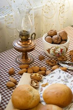 A vintage oil lamp on a checkered tablecloth with almonds, walnuts, and pastries, evoking a rustic kitchen feel.
