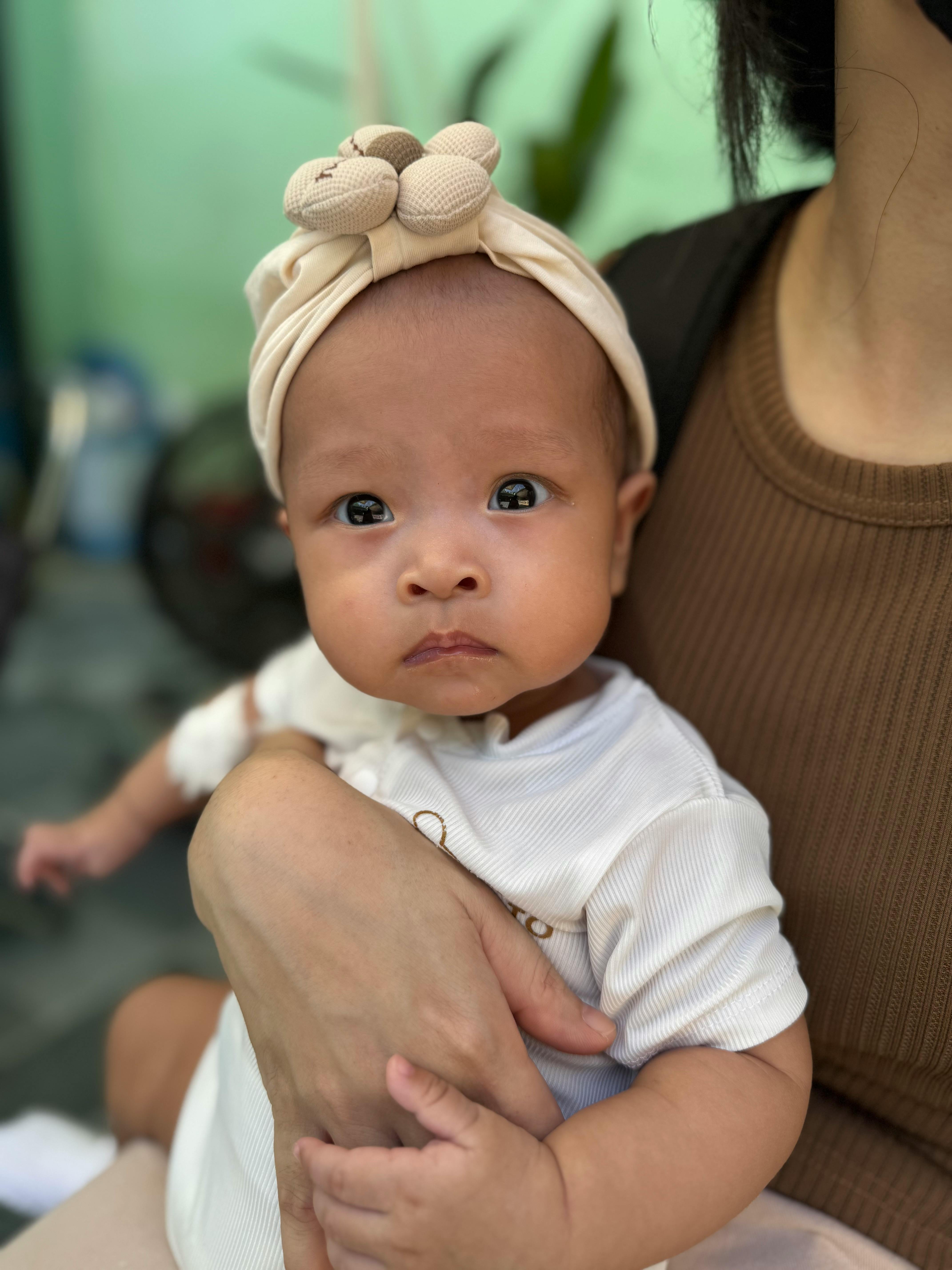 Gratis Primo piano di un grazioso neonato con un copricapo, tenuto in braccio dalla madre in Vietnam. Foto a disposizione