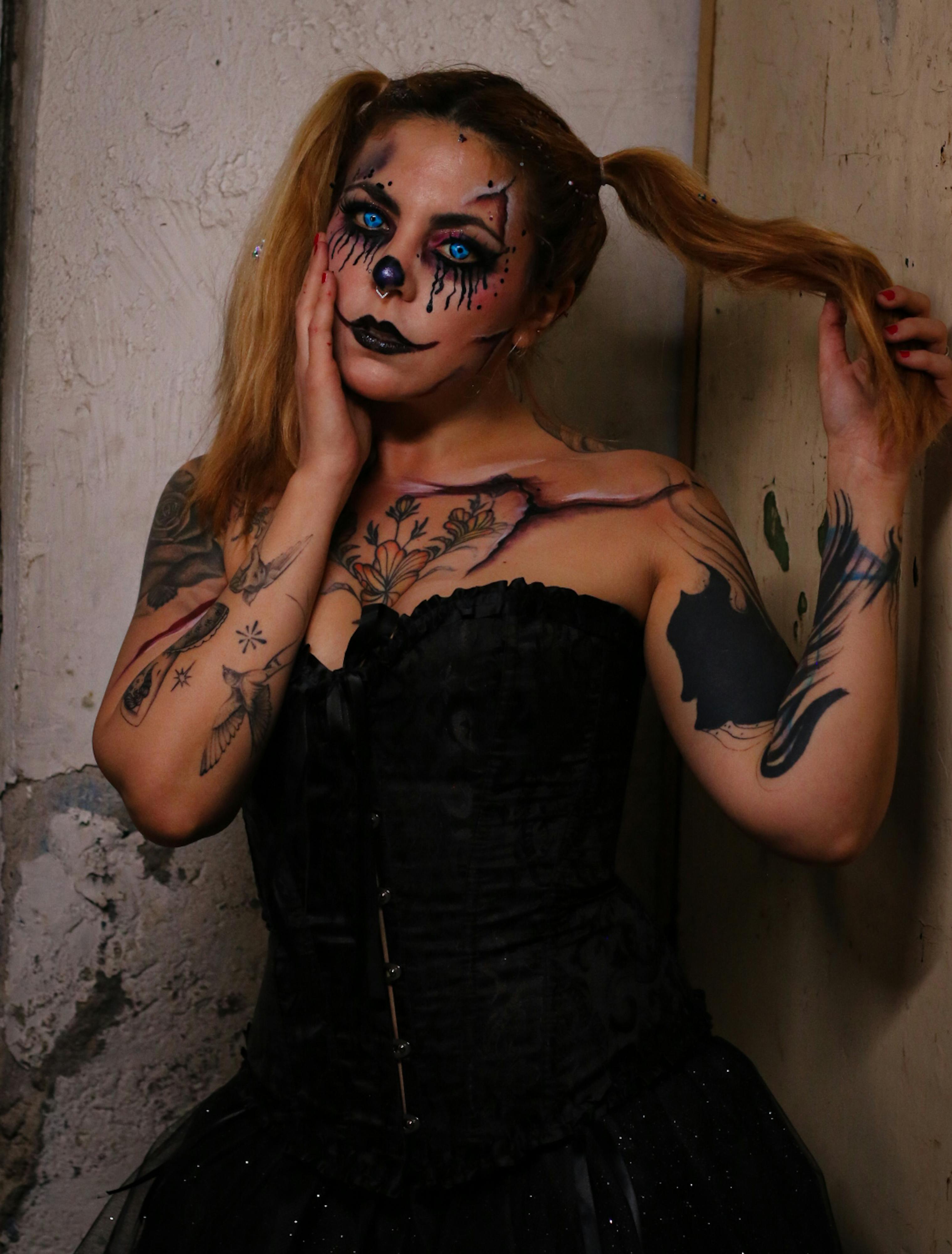 Ücretsiz Karmaşık yüz boyalarıyla gotik palyaço kostümü giymiş, sert bir kentsel ortamda bulunan bir kadın. Stok Fotoğraflar