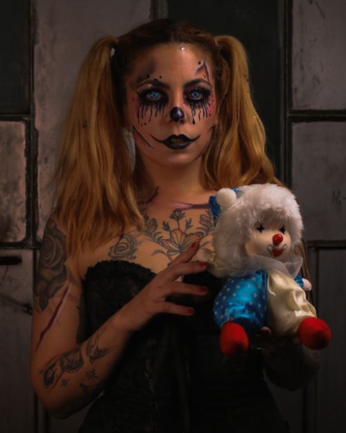 Free Woman in clown makeup holding a teddy bear in a dark room, creating a spooky atmosphere. Stock Photo