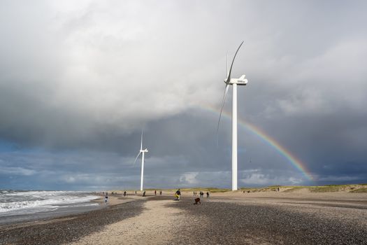 Scenic view of wind turbines on Hvide Sande beach under a rainbow.