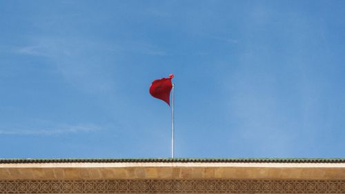 Free Red Moroccan flag atop building with ornate patterns against clear blue sky. Stock Photo