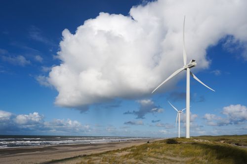Free Wind turbines on a beach in Hvide Sande, Denmark, with a clear blue sky and coastal landscape. Stock Photo