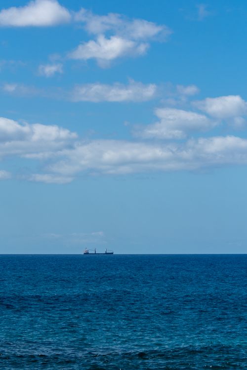 Free Serene ocean view with a distant cargo ship on the horizon under a partly cloudy sky. Stock Photo