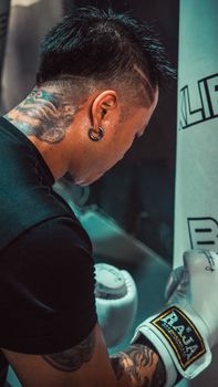 A focused boxer with tattoos and gloves practicing indoors at a punching bag.