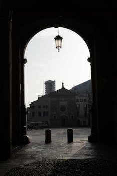 Silhouette view through an archway framing a historic building in a European town square.