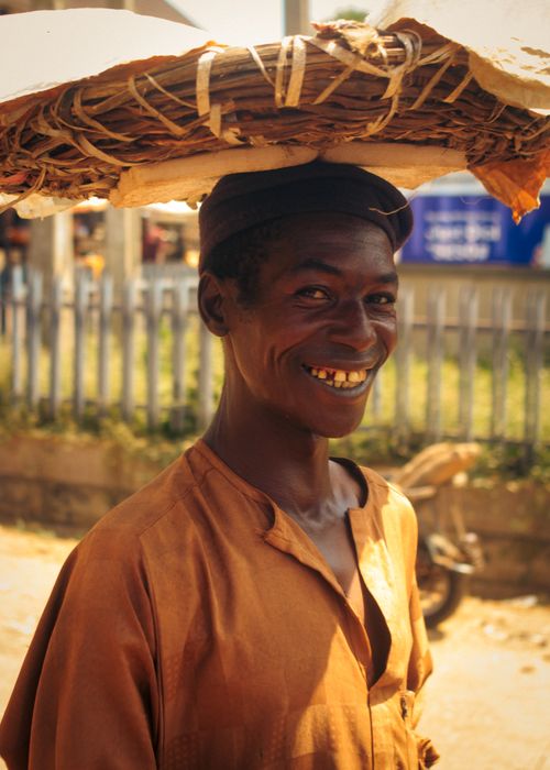 Free Portrait of a smiling street vendor balancing goods outdoors on a sunny day. Stock Photo