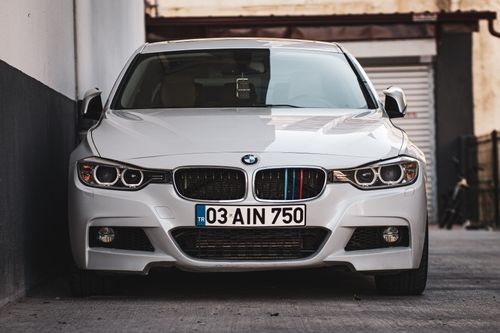 Free White BMW car parked in a narrow alley, showcasing its front grille and headlights. Stock Photo