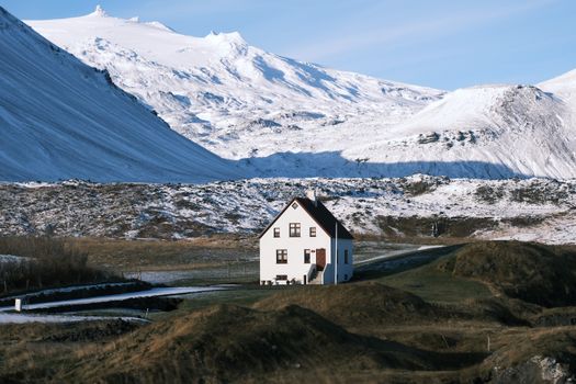 A lone white house nestled in Iceland's majestic snow-covered mountainscape.