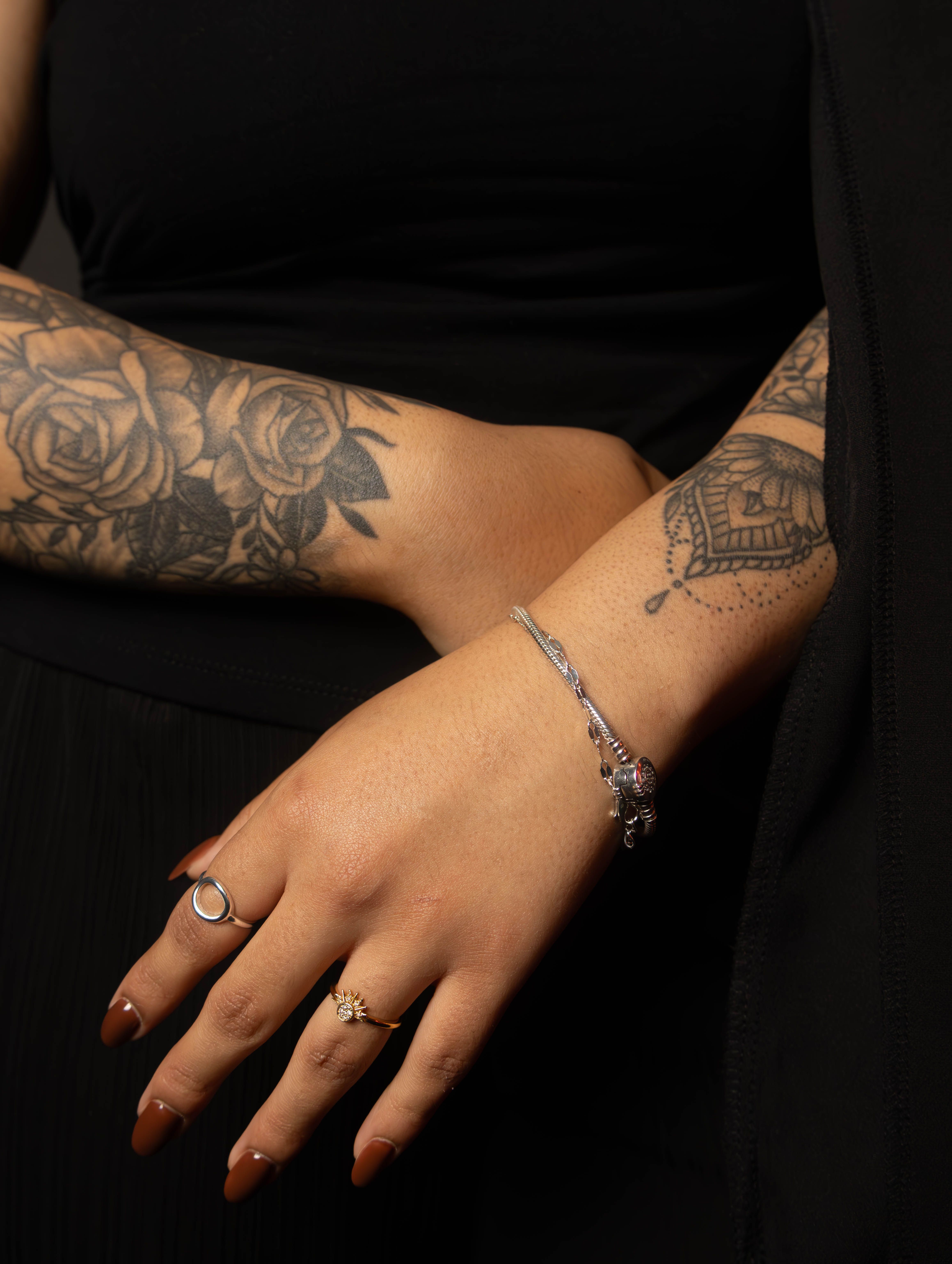 Close-up of tattooed arms adorned with rings and bracelets, showcasing intricate designs.