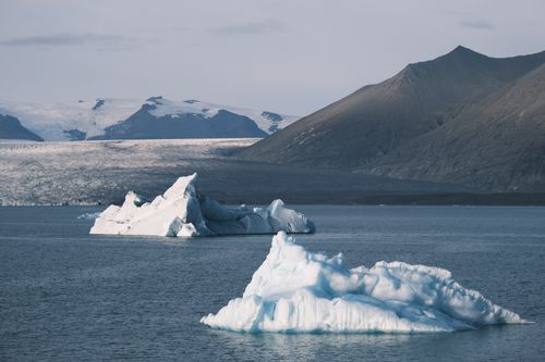 Free Pristine icebergs float in glacial waters against rugged Icelandic mountains, captured in natural daylight. Stock Photo