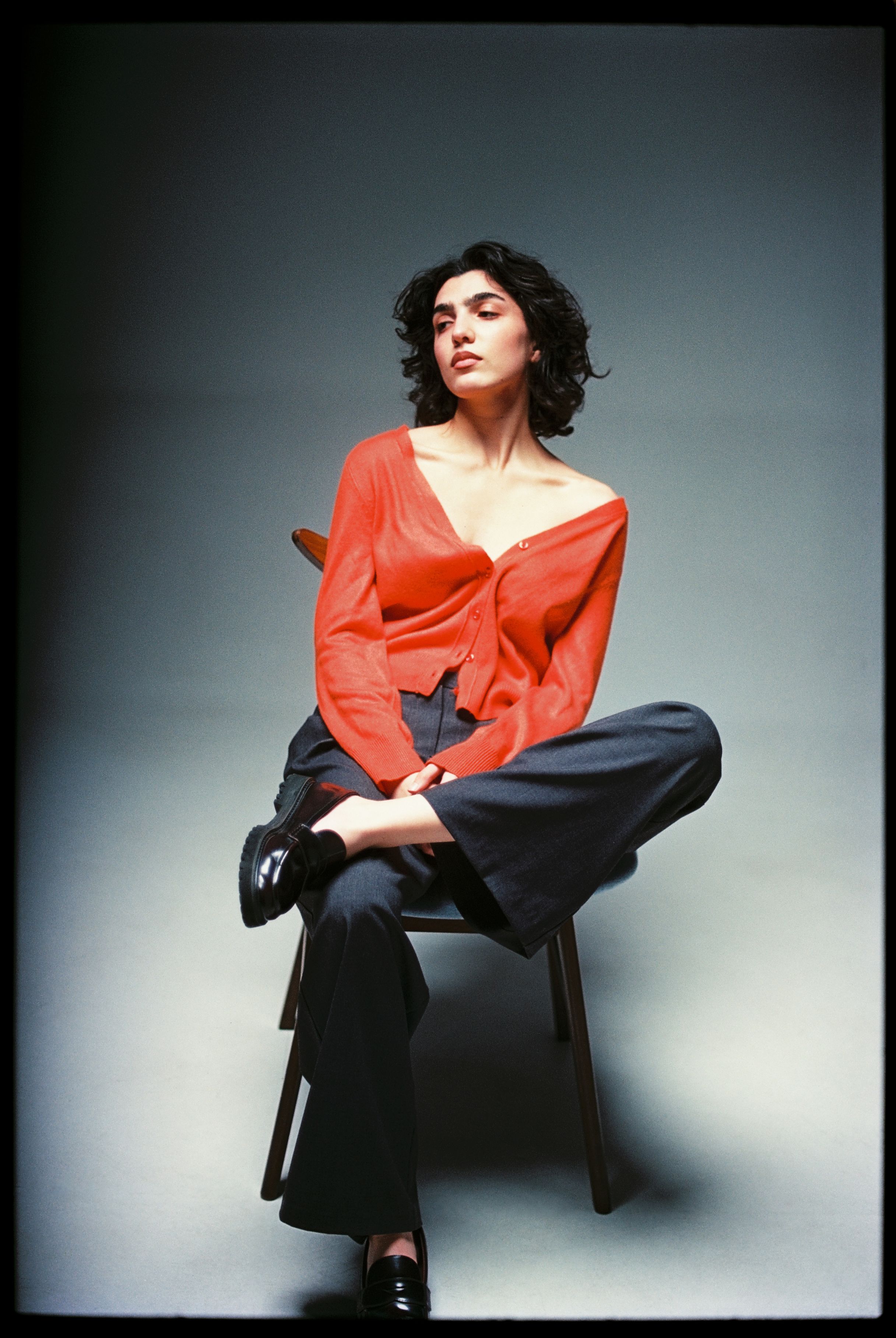 Elegant woman in a red cardigan poses confidently in a studio setting.