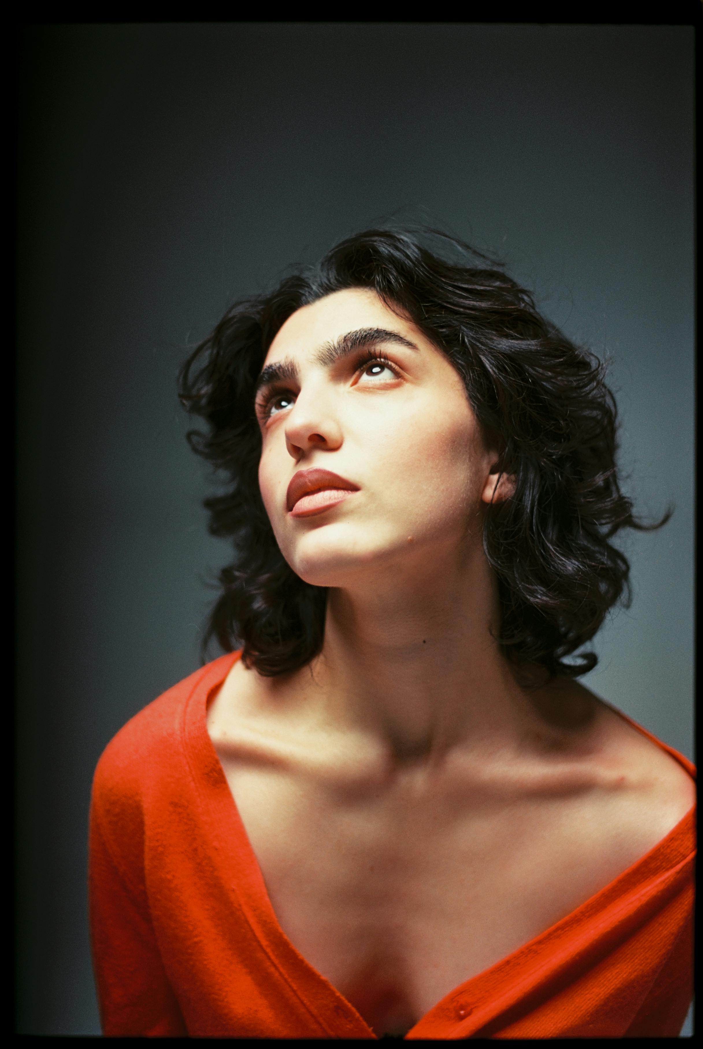 Elegant studio portrait of a young woman gazing upward, wearing a bold red top. Captures beauty and introspection.