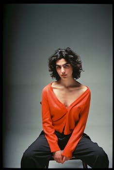 Fashion portrait of a confident woman in an orange cardigan sitting in a studio.