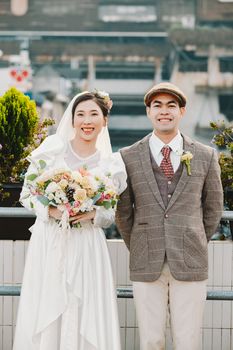 Charming couple in vintage attire posing on a rooftop, holding a bridal bouquet.