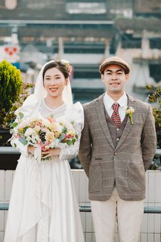 Charming couple in vintage wedding attire posing outdoors with a bouquet.