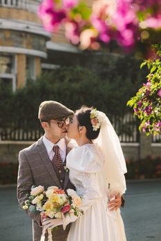 A stylish couple kissing at an outdoor wedding surrounded by flowers.