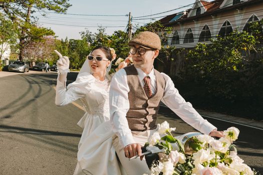 Vintage-styled couple on a bike, outdoors on a sunny day, celebrating their wedding.