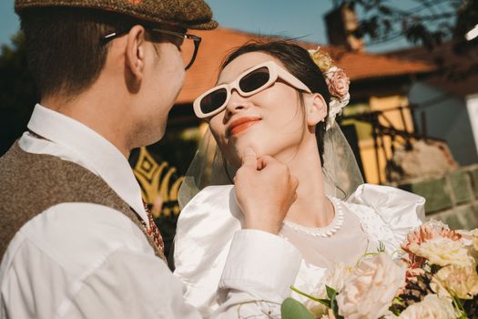 Stylish couple with retro flair enjoy a sunny outdoor wedding moment.