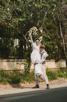 A happy couple in vintage attire celebrating their wedding outdoors with a joyful pose and bouquet.