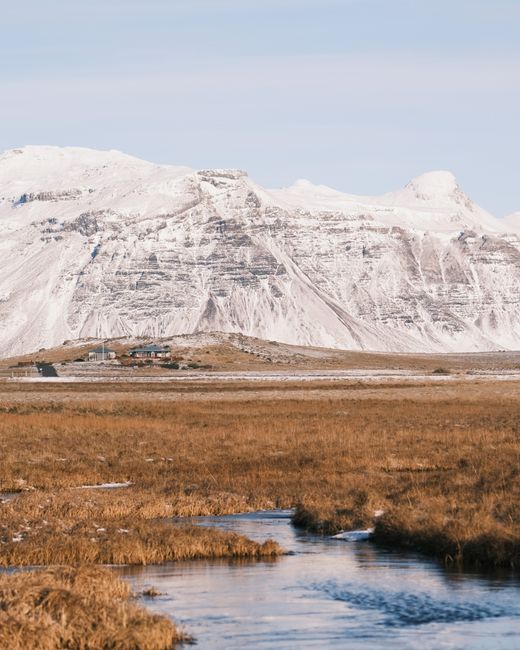 Stunning view of Iceland's snowy mountains with a serene river and vast plains.