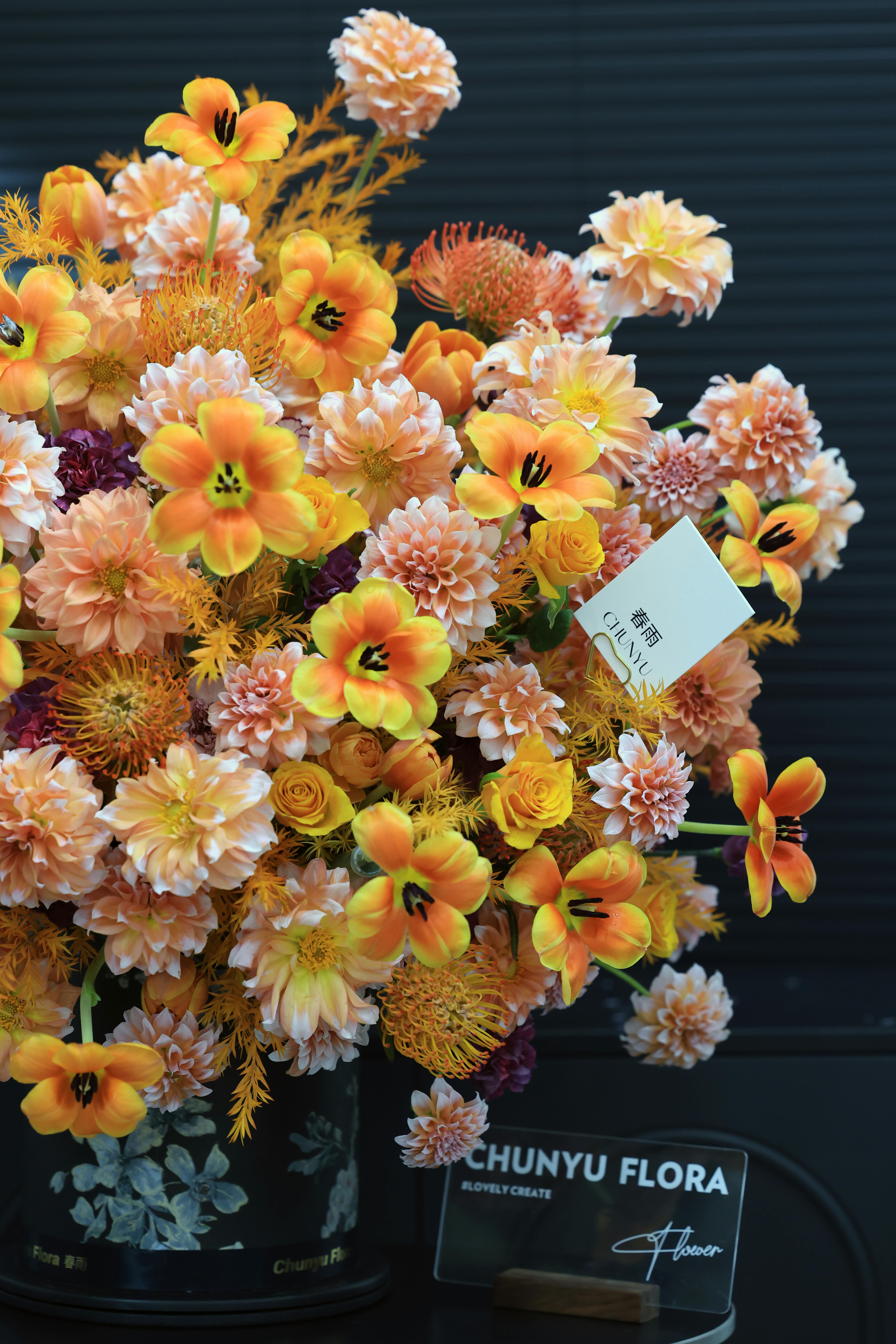 A stunning arrangement of orange and peach artificial flowers in a black vase with floral patterns.