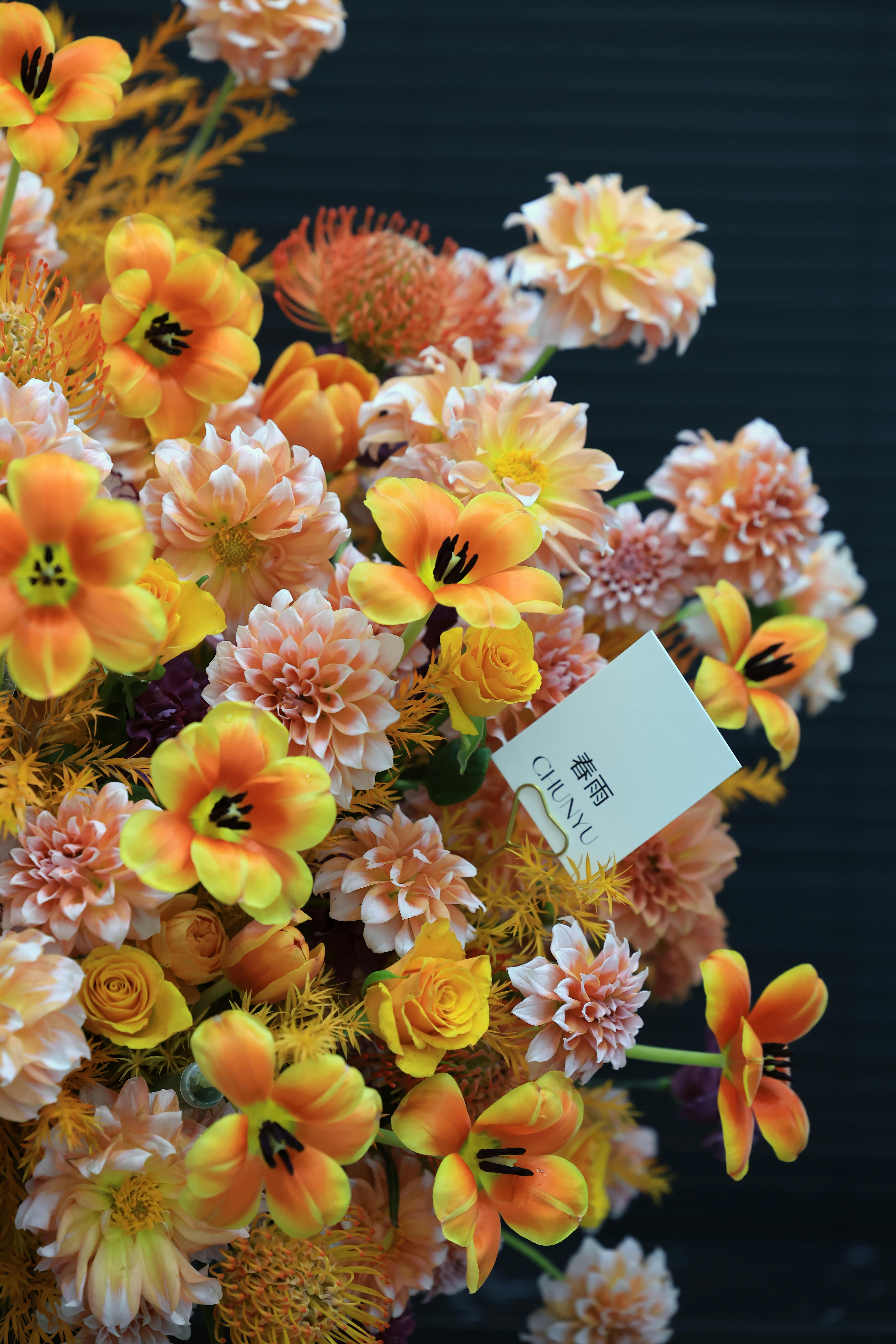 A bouquet of vibrant orange and yellow flowers with a visible card set against a dark background.